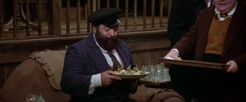 Movie still from “Popeye” (1980), directed by Robert Altman – A man in a hat is holding a plate of food; Medium shot, High angle