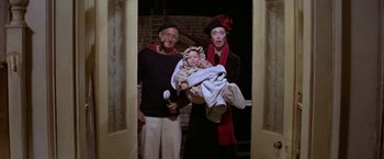 Movie still from “Popeye” (1980), directed by Robert Altman – An old man holding a baby and a young woman; Medium shot, High angle
