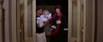Movie still from “Popeye” (1980), directed by Robert Altman – A man holding a baby and a woman in a black dress; Medium shot, Low angle