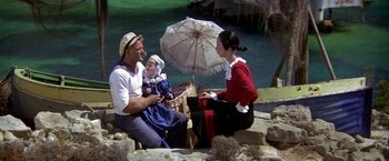 Movie still from “Popeye” (1980), directed by Robert Altman – A man , woman and child sitting under an umbrella; Wide shot, High angle