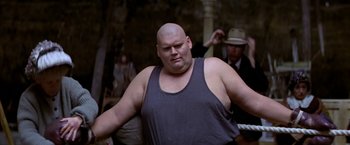 Movie still from “Popeye” (1980), directed by Robert Altman – A man with a bald head is standing in front of a crowd; Medium shot, Low angle