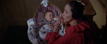 Movie still from “Popeye” (1980), directed by Robert Altman – A woman feeding a bottle to a baby in a bassinet; Medium shot, High angle