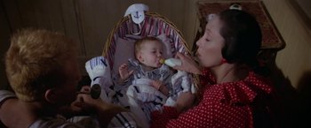 Movie still from “Popeye” (1980), directed by Robert Altman – A woman feeding a baby in a bassinet; Close Up shot, High angle