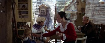 Movie still from “Popeye” (1980), directed by Robert Altman – Two people are sitting at a table outside; Medium shot, High angle