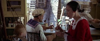Movie still from “Popeye” (1980), directed by Robert Altman – A man and a woman sitting at a table; Medium shot, High angle