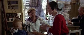 Movie still from “Popeye” (1980), directed by Robert Altman – A man and a woman are sitting at a table talking; Medium shot, Over the shoulder angle
