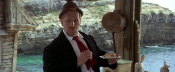 Movie still from “Popeye” (1980), directed by Robert Altman – A man holding a piece of pizza in his hand; Medium shot, Low angle