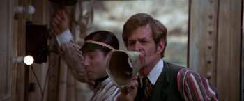Movie still from “Popeye” (1980), directed by Robert Altman – A man holding a paper horn in front of another man; Close Up shot, Low angle