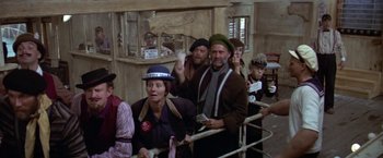 Movie still from “Popeye” (1980), directed by Robert Altman – A group of people standing next to each other in a room; Wide shot, High angle