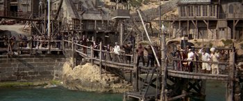 Movie still from “Popeye” (1980), directed by Robert Altman – A group of people walking across a wooden bridge; Extreme Wide shot, High angle