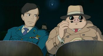Movie still from “Porco Rosso” (1992), directed by Hayao Miyazaki – A man and a woman sitting next to each other in front of a camera; Medium shot, Low angle