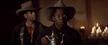 Movie still from “Posse” (1993), directed by Mario Van Peebles – A man in a hat and glasses holding a tea pot; Close Up shot, Over the shoulder angle