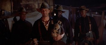 Movie still from “Posse” (1993), directed by Mario Van Peebles – A man holding a stuffed animal while standing next to another man; Medium shot, Low angle