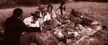 Movie still from “Posse” (1993), directed by Mario Van Peebles – A group of people sitting on a blanket on the grass; Medium shot, High angle