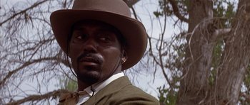 Movie still from “Posse” (1993), directed by Mario Van Peebles – A man wearing a brown hat and a suit; Close Up shot, Low angle