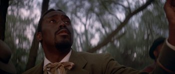 Movie still from “Posse” (1993), directed by Mario Van Peebles – A man wearing a suit and bow tie looking up at the sky; Close Up shot, Low angle