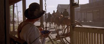 Movie still from “Posse” (1993), directed by Mario Van Peebles – A man standing in front of a group of people on horses; Wide shot, Over the shoulder angle