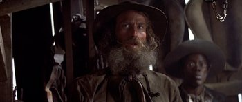 Movie still from “Posse” (1993), directed by Mario Van Peebles – A man with a long beard wearing a hat; Close Up shot, Low angle