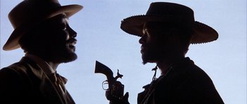 Movie still from “Posse” (1993), directed by Mario Van Peebles – A man holding a gun in his right hand and another man holding a revolver in his left hand; Close Up shot, Low angle