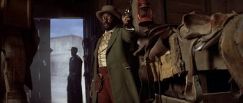 Movie still from “Posse” (1993), directed by Mario Van Peebles – A man with a gun in his hand and wearing a cowboy hat; Medium shot, Low angle