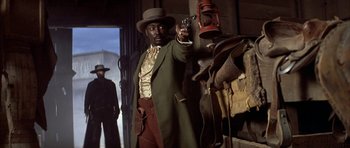 Movie still from “Posse” (1993), directed by Mario Van Peebles – A man holding a gun while standing in a room; Medium shot, Low angle