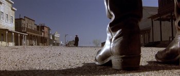 Movie still from “Posse” (1993), directed by Mario Van Peebles – A person standing on the side of a road with a cowboy hat on; Wide shot, Low angle