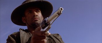 Movie still from “Posse” (1993), directed by Mario Van Peebles – A man holding a gun while wearing a cowboy hat; Close Up shot, Low angle