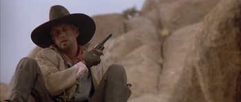 Movie still from “Posse” (1993), directed by Mario Van Peebles – A man holding a gun while sitting on the ground; Close Up shot, Low angle