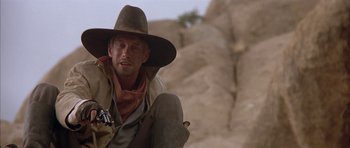 Movie still from “Posse” (1993), directed by Mario Van Peebles – A man in a cowboy hat sitting in front of a rock wall; Close Up shot, Low angle