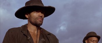 Movie still from “Posse” (1993), directed by Mario Van Peebles – A person wearing a hat with a sky in the background; Close Up shot, Low angle