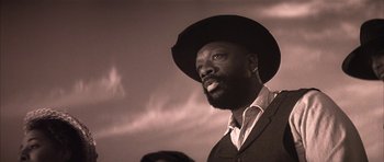 Movie still from “Posse” (1993), directed by Mario Van Peebles – A man with a beard wearing a hat and a suit; Close Up shot, Low angle