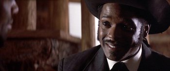 Movie still from “Posse” (1993), directed by Mario Van Peebles – A person wearing a suit and a cowboy hat; Close Up shot, Low angle