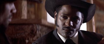 Movie still from “Posse” (1993), directed by Mario Van Peebles – A man in a black suit and a black hat; Close Up shot, Low angle