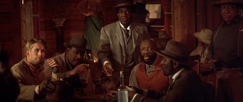 Movie still from “Posse” (1993), directed by Mario Van Peebles – A group of men sitting at a table with drinks; Medium shot, Low angle