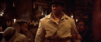 Movie still from “Posse” (1993), directed by Mario Van Peebles – A man wearing a hat and a trench coat in a bar; Medium shot, Over the shoulder angle