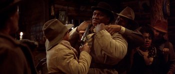 Movie still from “Posse” (1993), directed by Mario Van Peebles – A group of men holding a gun in a room; Medium shot, Low angle