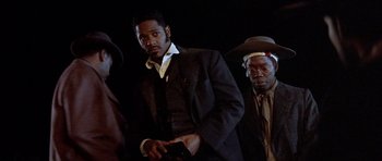 Movie still from “Posse” (1993), directed by Mario Van Peebles – A group of men standing next to each other in a dark room; Medium shot, Low angle