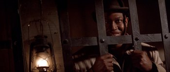 Movie still from “Posse” (1993), directed by Mario Van Peebles – A man holding onto a metal bar in front of his face; Close Up shot, Low angle