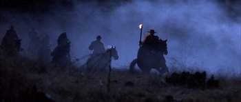 Movie still from “Posse” (1993), directed by Mario Van Peebles – A group of people riding horses through a field; Wide shot, Low angle