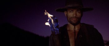 Movie still from “Posse” (1993), directed by Mario Van Peebles – A man in a cowboy hat holding a burning candle; Close Up shot, Low angle