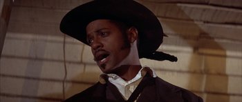 Movie still from “Posse” (1993), directed by Mario Van Peebles – A man wearing a black hat and a white shirt; Close Up shot, Low angle
