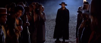 Movie still from “Posse” (1993), directed by Mario Van Peebles – A group of people standing in the dark; Wide shot, Over the shoulder angle