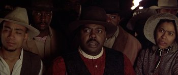 Movie still from “Posse” (1993), directed by Mario Van Peebles – A group of men standing next to each other in a dark room; Close Up shot, Low angle