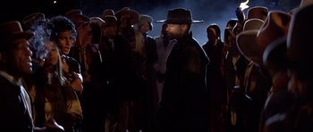 Movie still from “Posse” (1993), directed by Mario Van Peebles – A group of people standing in the dark wearing hats; Medium shot, Over the shoulder angle