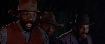 Movie still from “Posse” (1993), directed by Mario Van Peebles – A group of men standing next to each other in a dark room; Close Up shot, Low angle