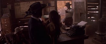 Movie still from “Posse” (1993), directed by Mario Van Peebles – A man in a hat is standing next to a woman in front of an old fashioned typewriter; Medium shot, Over the shoulder angle