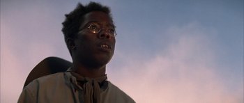 Movie still from “Posse” (1993), directed by Mario Van Peebles – A man with glasses looking up into the sky; Close Up shot, Low angle