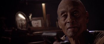 Movie still from “Posse” (1993), directed by Mario Van Peebles – An older man holding a remote control in his hand; Close Up shot, Low angle
