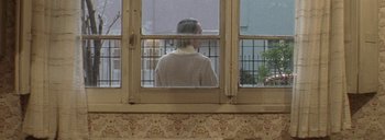 Movie still from “Post Mortem” (2010), directed by Pablo Larraín – A person looking out of a window; Medium shot, Over the shoulder angle
