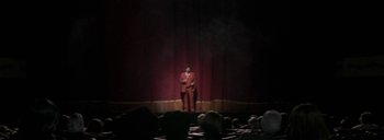 Movie still from “Post Mortem” (2010), directed by Pablo Larraín – A man in a red suit sitting in front of an audience; Wide shot, Low angle
